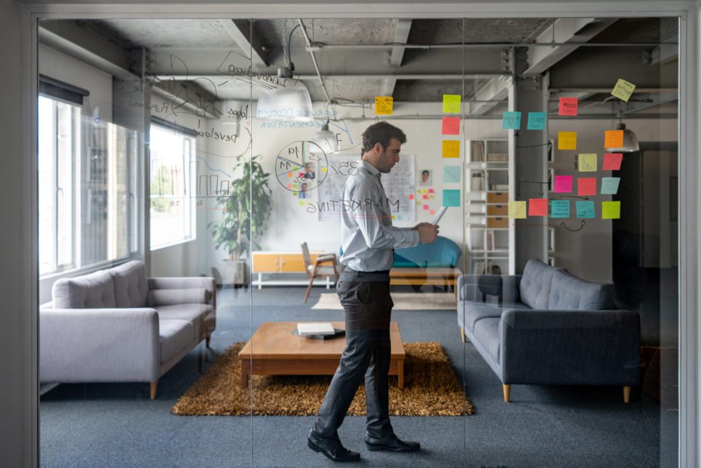 A businessman preparing for a business meeting with sticky notes on the transparent board in his office.